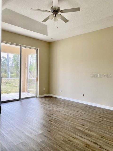 unfurnished room featuring a ceiling fan, baseboards, dark wood-style flooring, a textured ceiling, and a raised ceiling