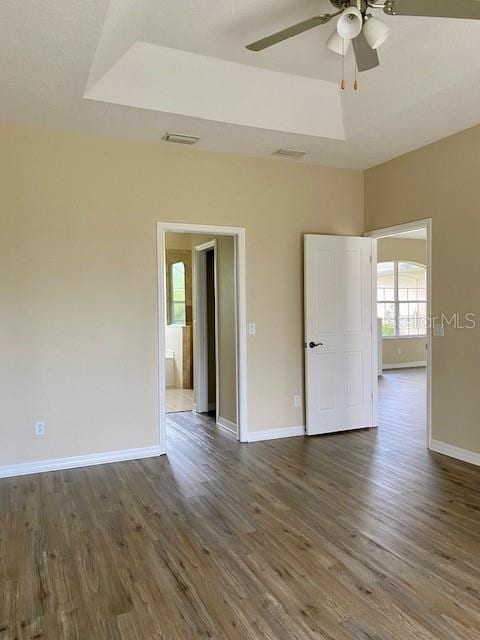 empty room featuring a ceiling fan, a raised ceiling, wood finished floors, and visible vents