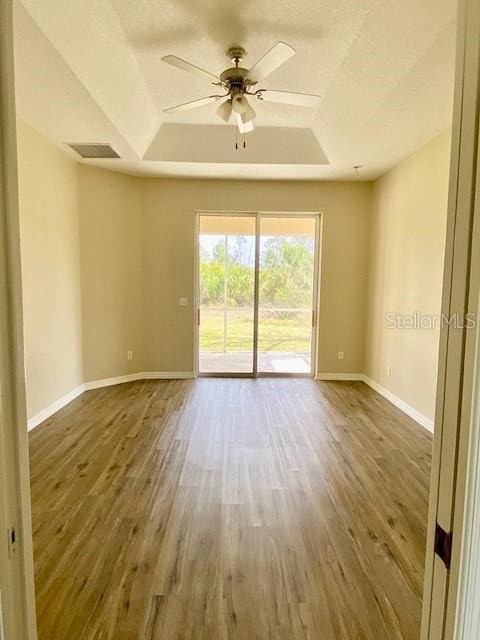 empty room with baseboards, a raised ceiling, and wood finished floors