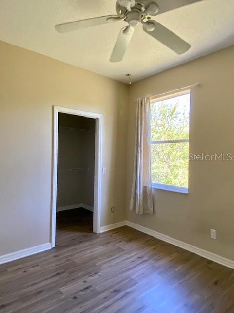 unfurnished bedroom with a walk in closet, wood finished floors, baseboards, and a closet