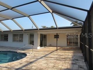 rear view of property featuring glass enclosure, an outdoor pool, and a patio