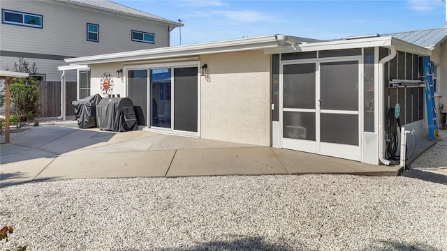 rear view of property with a sunroom, a patio area, fence, and stucco siding