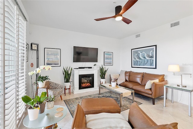 living room with light tile patterned floors, visible vents, a ceiling fan, and a glass covered fireplace