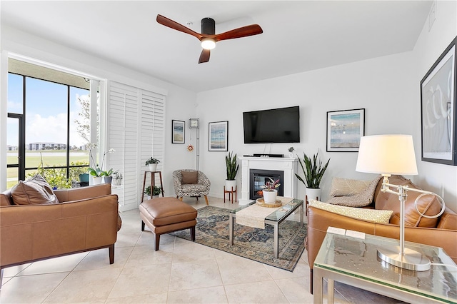 living room with light tile patterned floors, a glass covered fireplace, and a ceiling fan