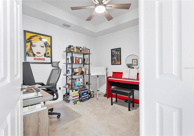 office space with carpet floors, a tray ceiling, visible vents, and a ceiling fan