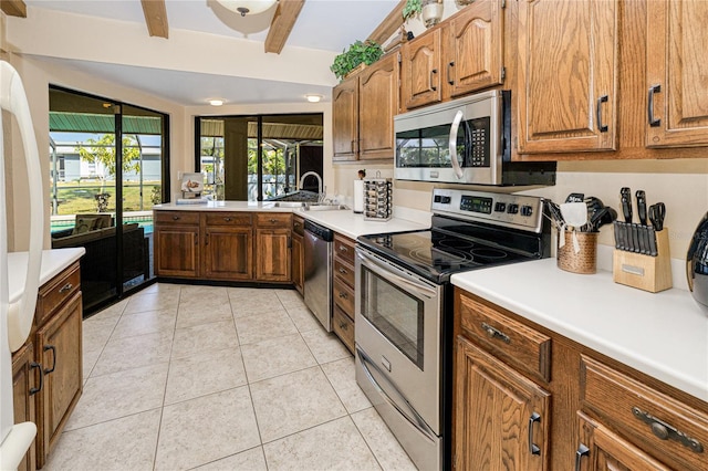 kitchen with light tile patterned floors, brown cabinetry, appliances with stainless steel finishes, beamed ceiling, and light countertops