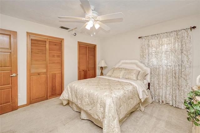 bedroom featuring light carpet, ceiling fan, visible vents, and two closets