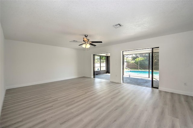 empty room featuring light wood finished floors, baseboards, visible vents, and a textured ceiling