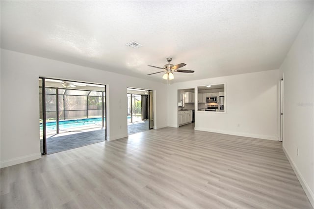 unfurnished living room featuring light wood-type flooring, ceiling fan, visible vents, and baseboards