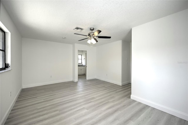 unfurnished room with visible vents, light wood-style floors, ceiling fan, a textured ceiling, and baseboards