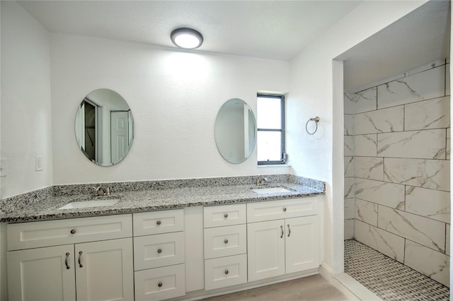 full bathroom with a sink, a tile shower, and double vanity