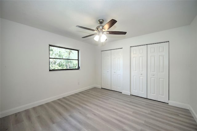 unfurnished bedroom with multiple closets, light wood finished floors, baseboards, and a ceiling fan