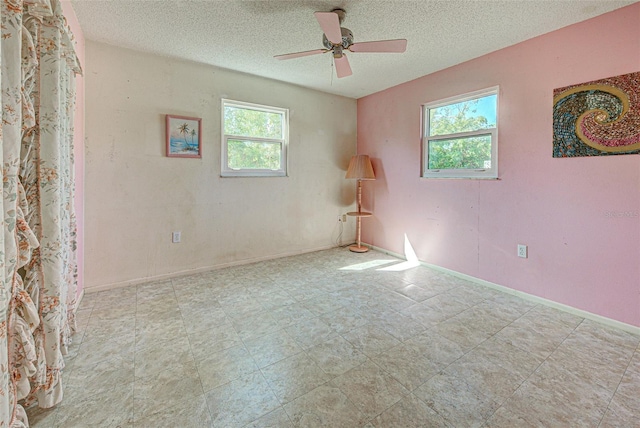 unfurnished room with a textured ceiling, a ceiling fan, a wealth of natural light, and baseboards