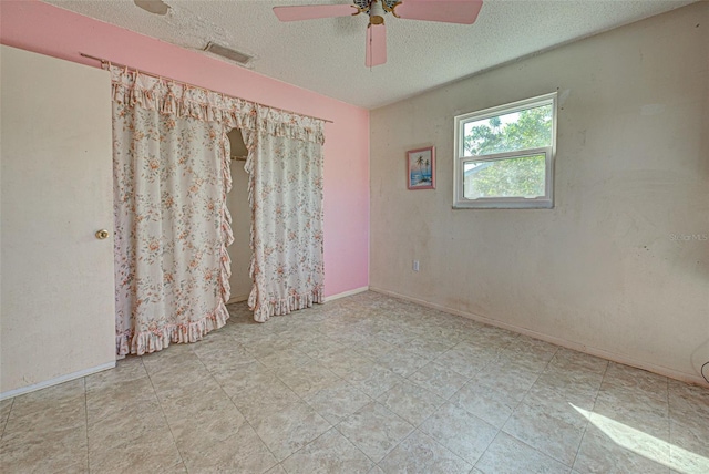 spare room with a textured ceiling, a ceiling fan, visible vents, and baseboards