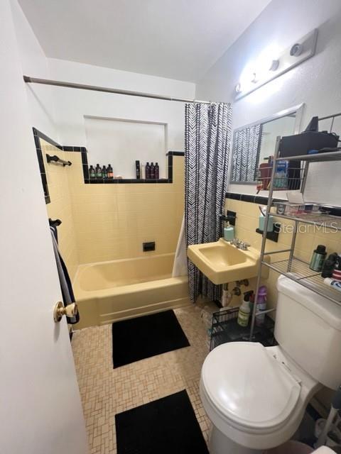 full bath featuring toilet, tile walls, a sink, and shower / tub combo with curtain