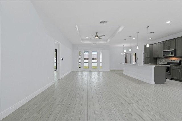 unfurnished living room with a ceiling fan, a raised ceiling, visible vents, and light wood-style flooring