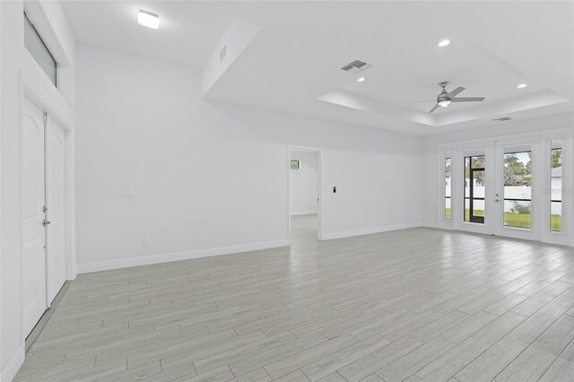 unfurnished living room featuring visible vents, baseboards, french doors, light wood finished floors, and a raised ceiling