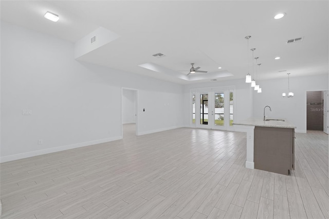 unfurnished living room featuring a raised ceiling, visible vents, light wood-style floors, a sink, and ceiling fan with notable chandelier