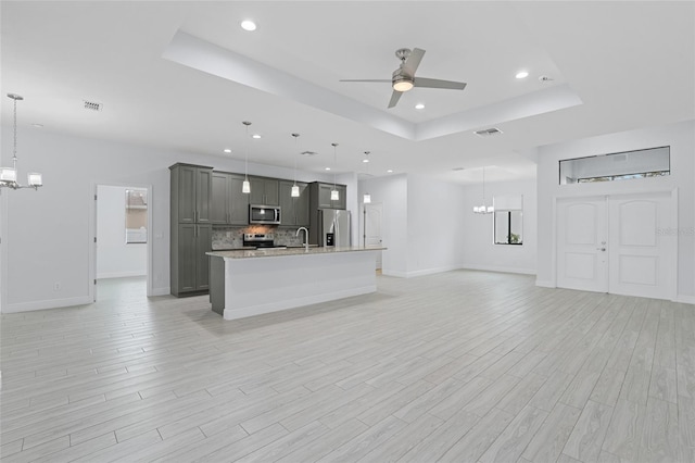 unfurnished living room featuring a raised ceiling, visible vents, light wood-style flooring, a sink, and ceiling fan with notable chandelier