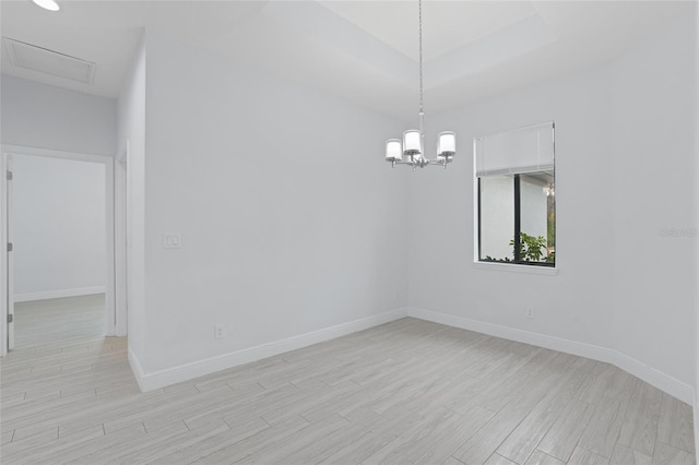 spare room featuring a raised ceiling, baseboards, and light wood finished floors