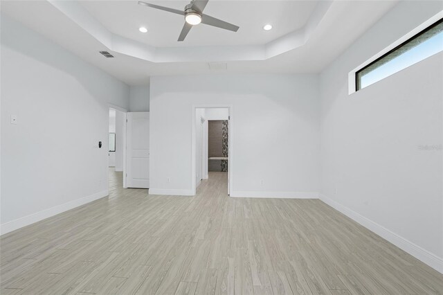 unfurnished bedroom with baseboards, visible vents, a tray ceiling, light wood-style floors, and recessed lighting