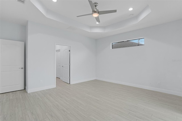 empty room with light wood-type flooring, baseboards, a raised ceiling, and a ceiling fan