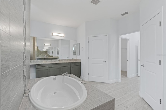 bathroom with tiled tub, vanity, visible vents, and baseboards