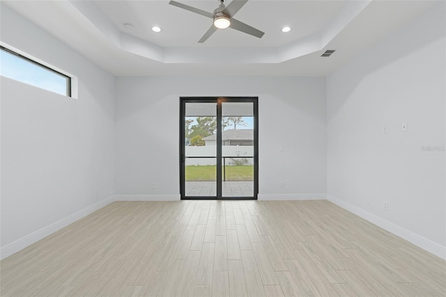 spare room featuring light wood-type flooring, plenty of natural light, baseboards, and a raised ceiling