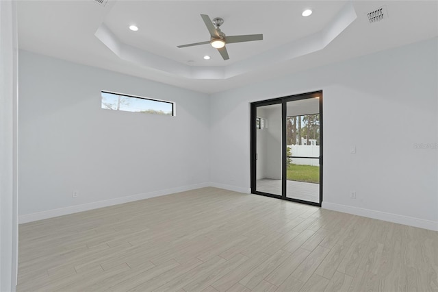 empty room featuring light wood-type flooring, a tray ceiling, plenty of natural light, and baseboards