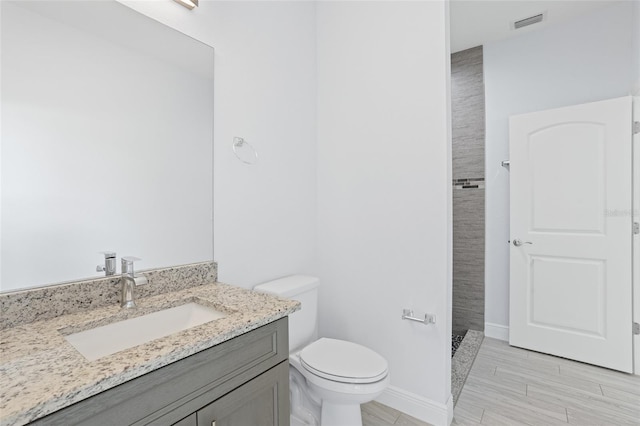 bathroom featuring baseboards, visible vents, toilet, a tile shower, and vanity