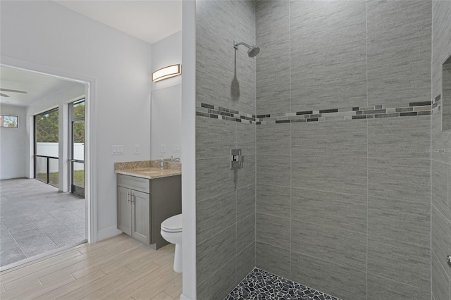 bathroom with toilet, wood finished floors, vanity, a ceiling fan, and tiled shower