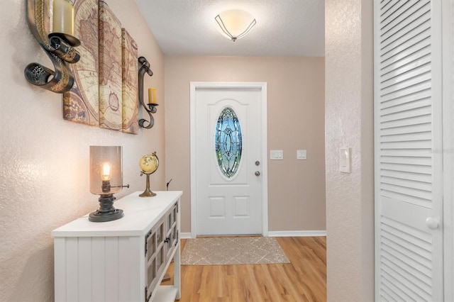 foyer featuring a textured ceiling, baseboards, and light wood-style floors