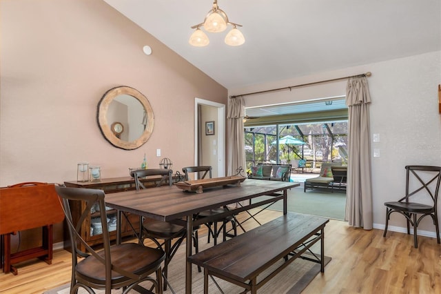 dining area featuring a notable chandelier, light wood-type flooring, baseboards, and vaulted ceiling