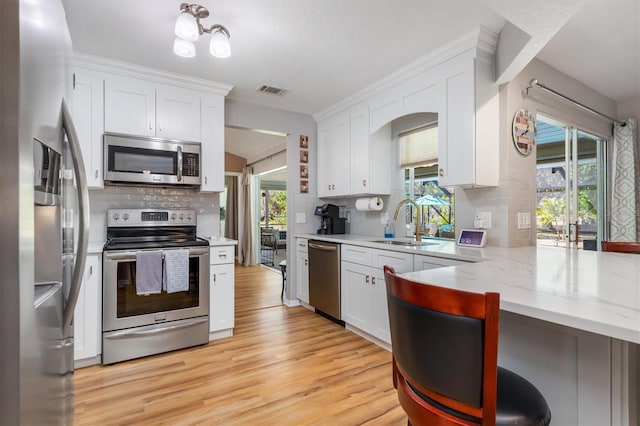 kitchen with white cabinetry, light wood-style floors, light stone countertops, and stainless steel appliances