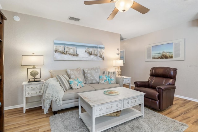 living room featuring wood finished floors, a ceiling fan, visible vents, and baseboards