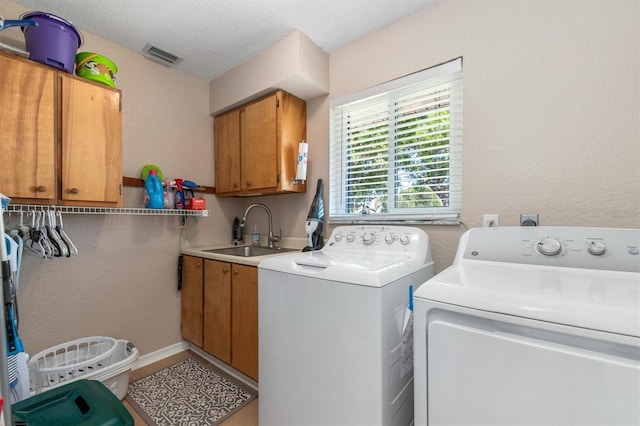 laundry room featuring visible vents, a textured wall, cabinet space, independent washer and dryer, and a sink