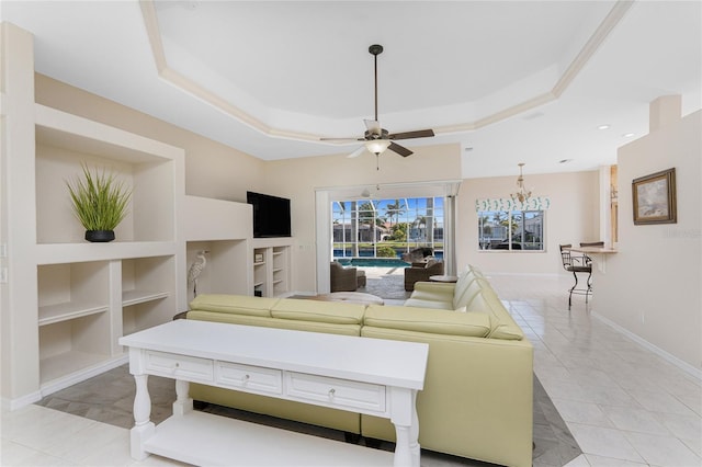 living area with built in features, a tray ceiling, light tile patterned floors, ceiling fan, and baseboards