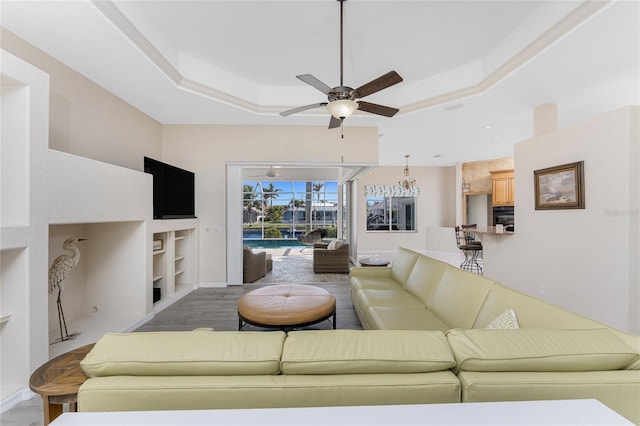 living room with baseboards, built in features, ceiling fan, a tray ceiling, and light wood-style floors