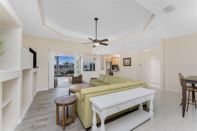 living room featuring arched walkways, a raised ceiling, visible vents, and baseboards