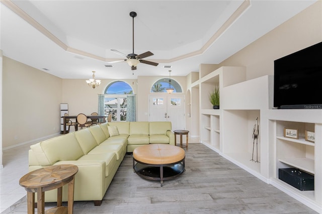 living room featuring built in shelves, ceiling fan with notable chandelier, wood finished floors, baseboards, and a raised ceiling