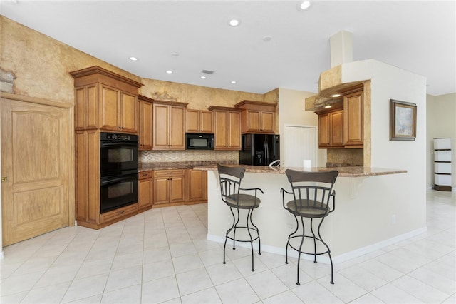 kitchen featuring a peninsula, black appliances, a breakfast bar, and brown cabinetry