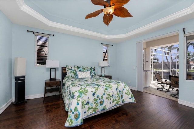 bedroom featuring access to exterior, a tray ceiling, multiple windows, and wood finished floors