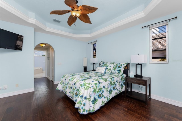 bedroom featuring baseboards, visible vents, arched walkways, a raised ceiling, and hardwood / wood-style floors