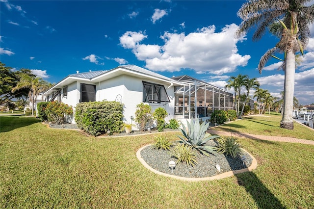 view of side of home featuring metal roof, glass enclosure, a lawn, and stucco siding