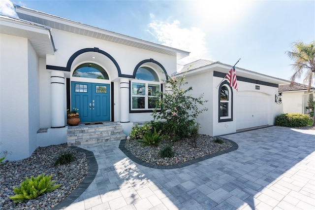 doorway to property with a garage, decorative driveway, and stucco siding