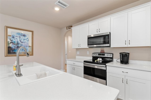 kitchen featuring visible vents, arched walkways, appliances with stainless steel finishes, light countertops, and a sink