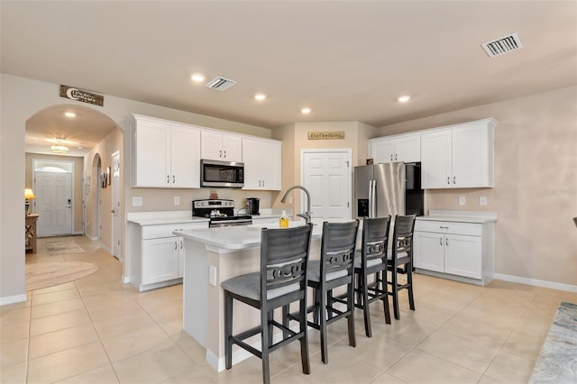 kitchen featuring visible vents, a kitchen island with sink, appliances with stainless steel finishes, and arched walkways