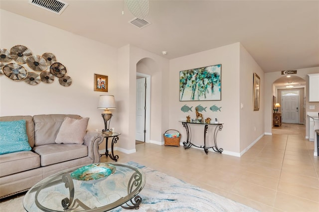 living area featuring arched walkways, light tile patterned floors, and visible vents