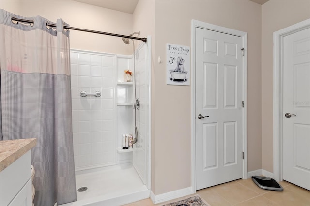 full bathroom with tiled shower, tile patterned flooring, vanity, and baseboards