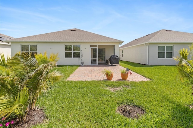 back of property with roof with shingles, stucco siding, a patio, and a lawn